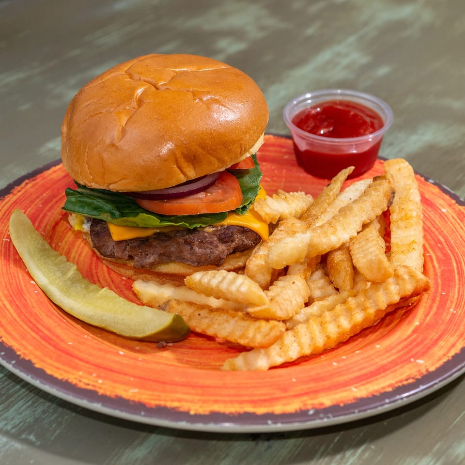 A cheeseburger with lettuce, tomato, and onion, served with crinkle-cut fries, ketchup, and a pickle spear.