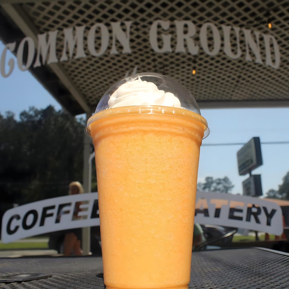 Orange Common Ground Coffee & Eatery smoothie with whipped cream on a patio table.