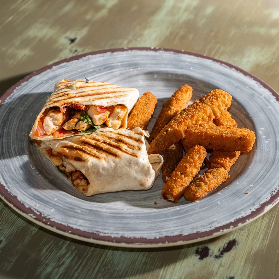 Grilled chicken wrap cut in half, served with a side of crispy fried mozzarella sticks on a plate.