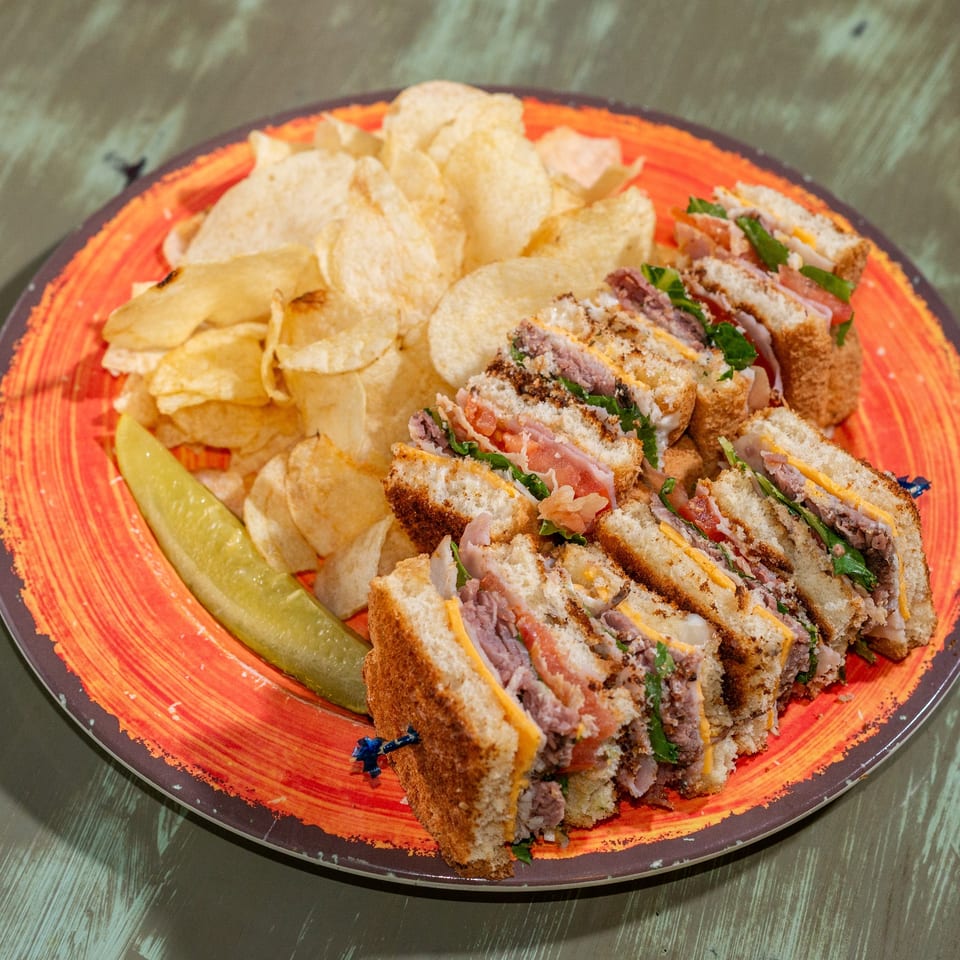 Club sandwich with chips and a pickle spear on an orange plate at Common Ground Coffee & Eatery.
