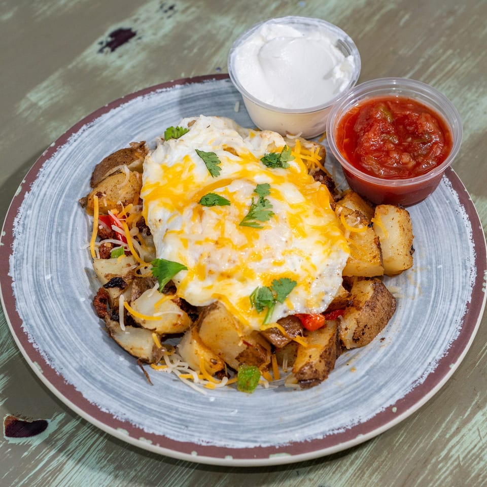 A breakfast skillet with potatoes, cheese, fried egg, cilantro, salsa, and sour cream.